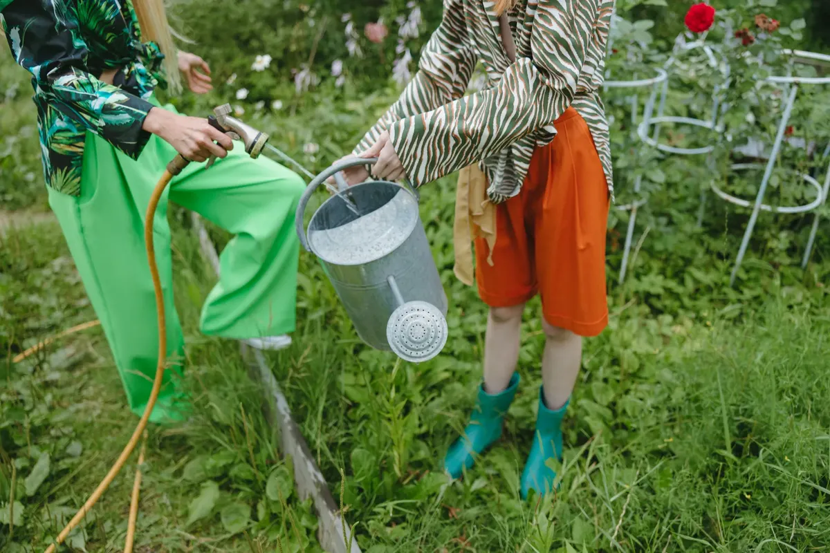 Two individuals filling a watering can with a hose in a vibrant garden setting, perfect for spring.
